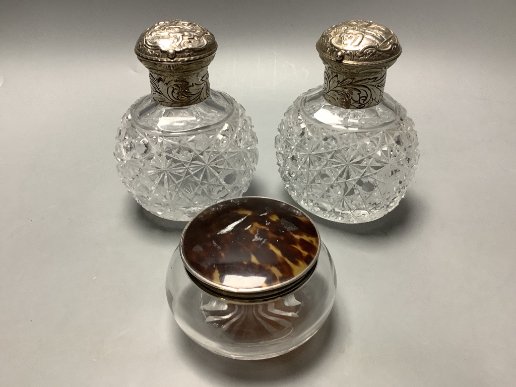 A pair of late Victorian silver mounted cut glass scent bottles, London, 1887, height 13.1 cm and a silver and tortoiseshell powder jar.